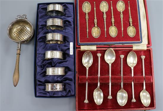 Two cased sets of silver spoons, a cased set of six silver napkin rings and a silver tea strainer on stand.